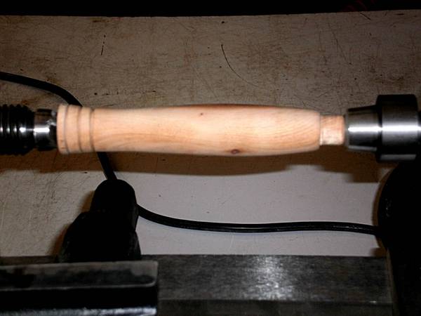 Wood handle on lathe with headstock and tail stock.